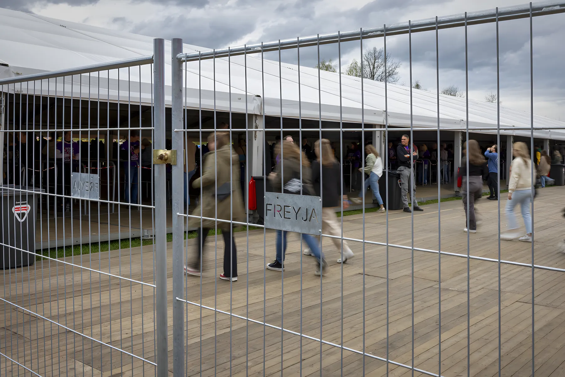 Bezoekers lopen langs open hekwerk met het Freyja-bord bij een festivaltent