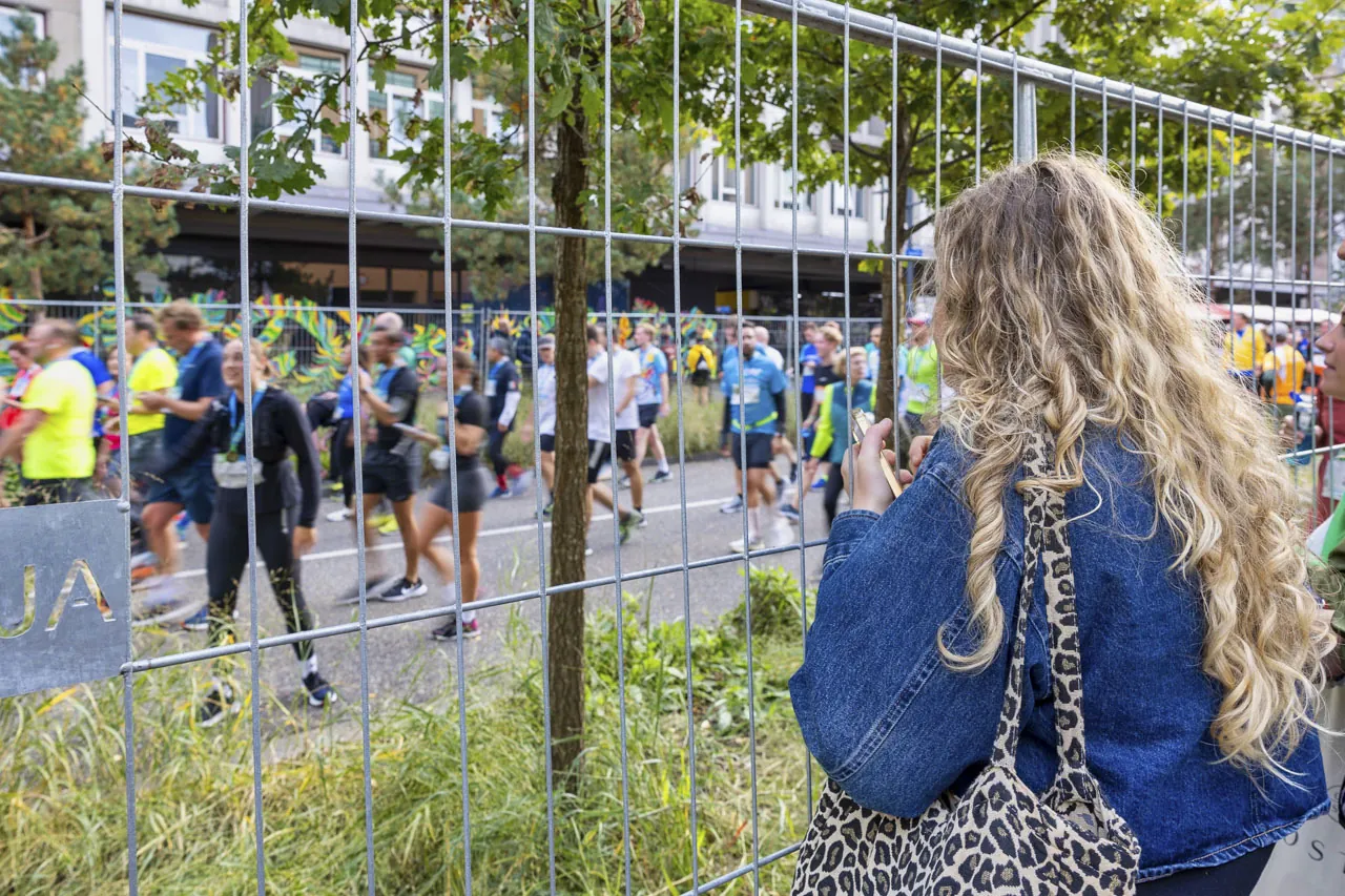 Toeschouwer kijkt door het hekwerk naar de marathon