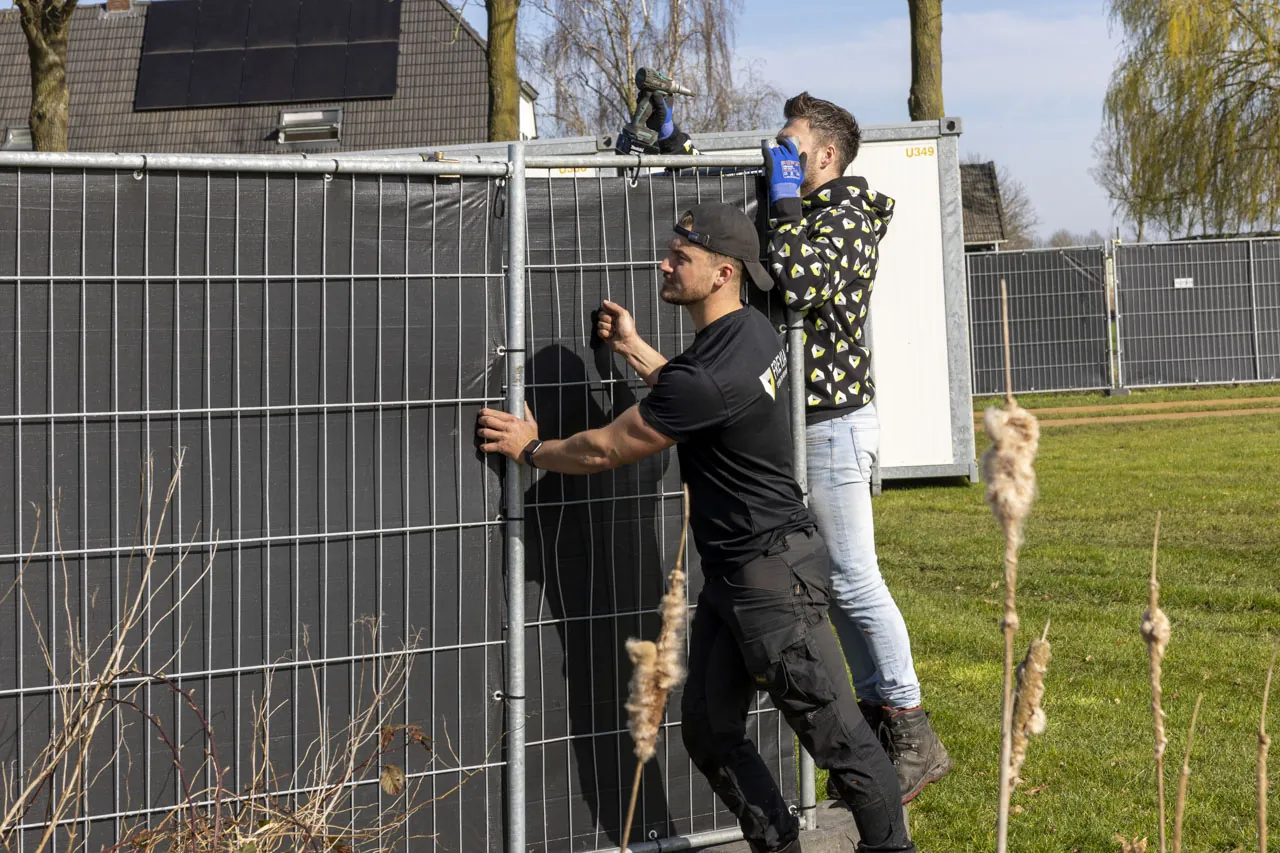 Hekwerkers plaatsen een zwart gezeild hek